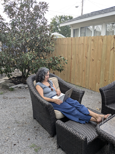Woman working on a computer outside while sitting on patio furniture with legs up